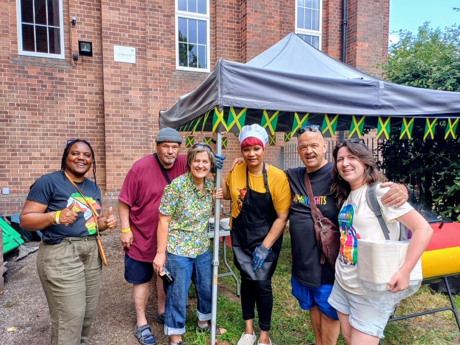 Team players by the Jerk Chicken stall. Yum! Photo of people standing by the Jerk Chicken stall.